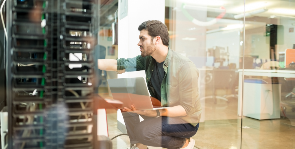 A network technician working on a laptop while configuring a server in a modern server room.